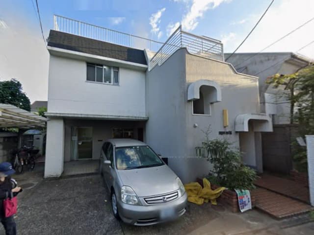 - シンプルで現代的な外観の住宅、駐車場に停まったシルバーの車、青空の下に建つ家の紹介