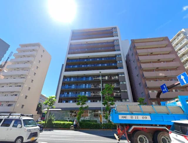 - 都会的な高層マンションの外観、周囲には他の建物や緑があり、晴れた青空の下にある風景