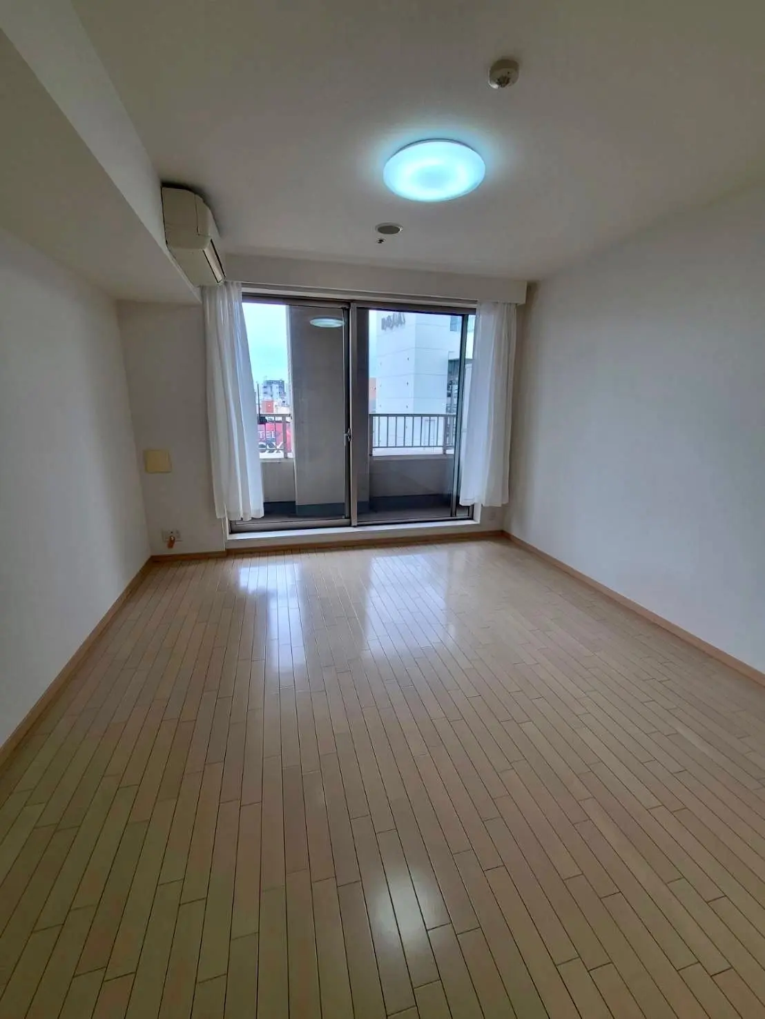 明るく広々とした空の部屋、ベージュ色のタイルフローリング、ベランダ付き、LED照明とエアコン完備のインテリア