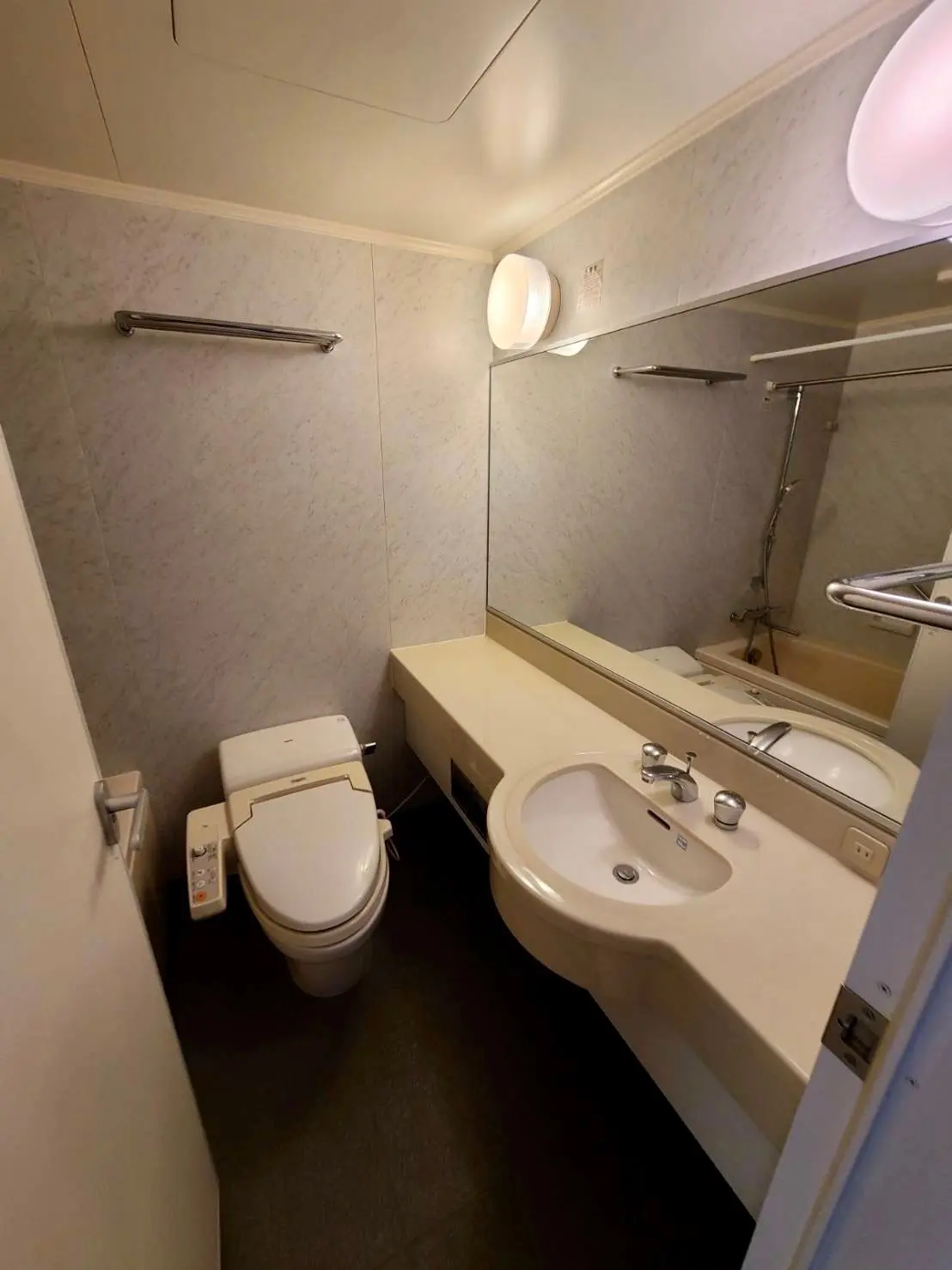 コンパクトなバスルーム、洗面台とトイレが一体型、暖色の照明と大理石風の壁