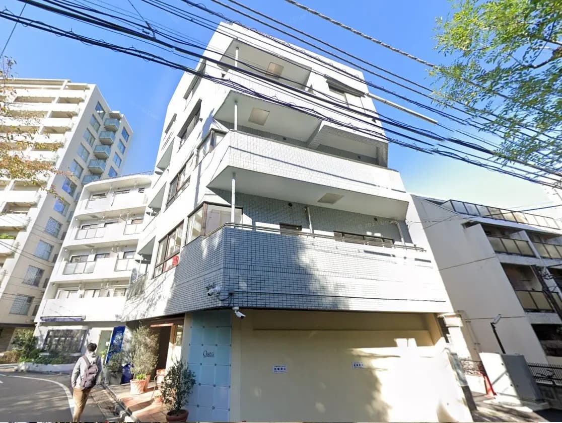都市の日当たりの良い角地にあるモダンなマンション、歩行者と街路樹が見える外観