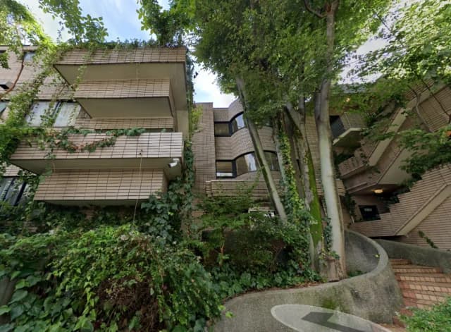 緑に囲まれたモダンなマンション外観、植物が這うバルコニーと曲線の階段