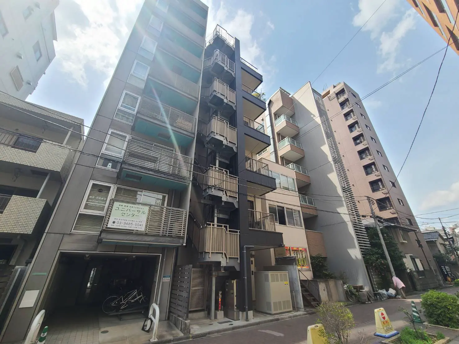 - 都市型アパートメントの外観、バルコニーのあるモダンなデザインと周囲の街並み、青空が広がる風景