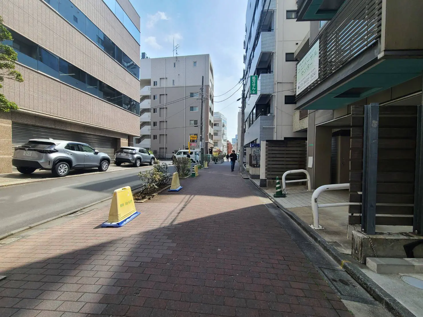 - 都市の歩道に沿って続く通り、並んだ車両と日差しの下にある商業ビルの風景