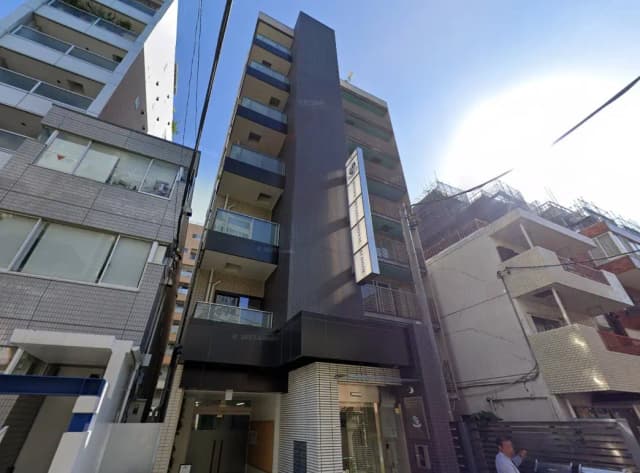 都会の狭い路地に建つモダンなマンションと周囲の建物、晴れた日の都市環境