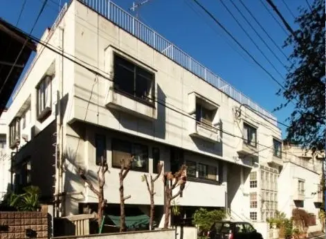 都市の住宅街にあるモダンなアパートビルの外観、晴天の下、冬期に剪定された木の前