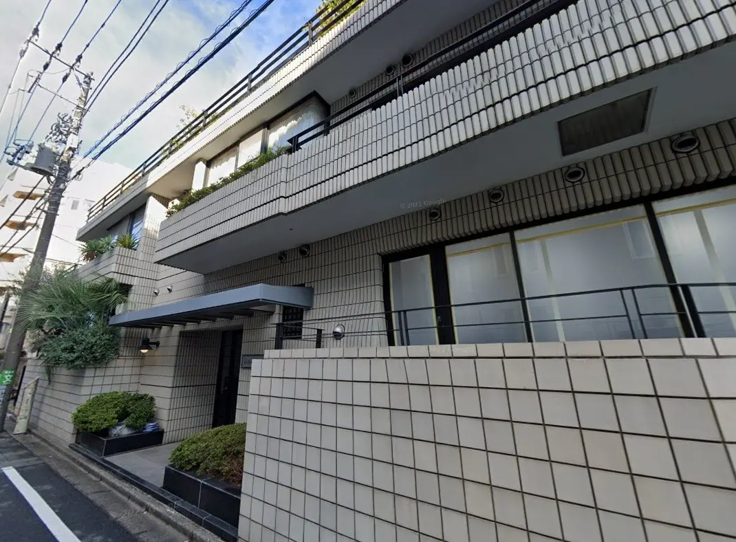 都市型マンションの外観、白いタイルとグリーンの植栽が特徴的なファサードデザイン