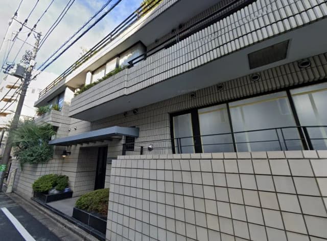 都市型マンションの外観、白いタイルとグリーンの植栽が特徴的なファサードデザイン