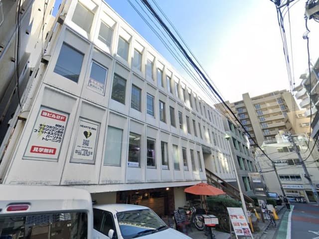 日本の都市部に位置するオフィスビルの外観、路上駐車車両と周辺のビジネスサインが見える