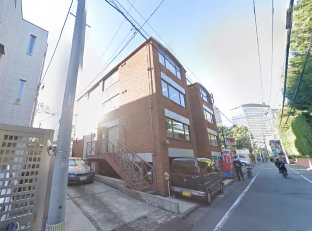 - 都市の街並みに立つレンガ造りのビル、周囲に駐車スペースと人が行き交う様子が見える風景