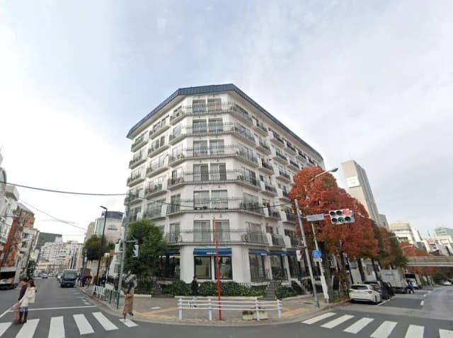 都市の交差点にあるモダンなマンション、広い歩道と周囲の樹木