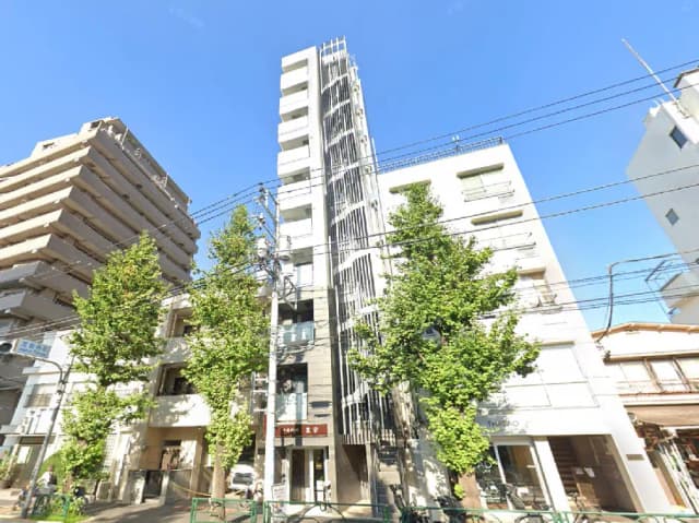 - 近代的な外観のビル群、青空の下に高さの異なる建物と手入れの行き届いた街路樹が並ぶ風景