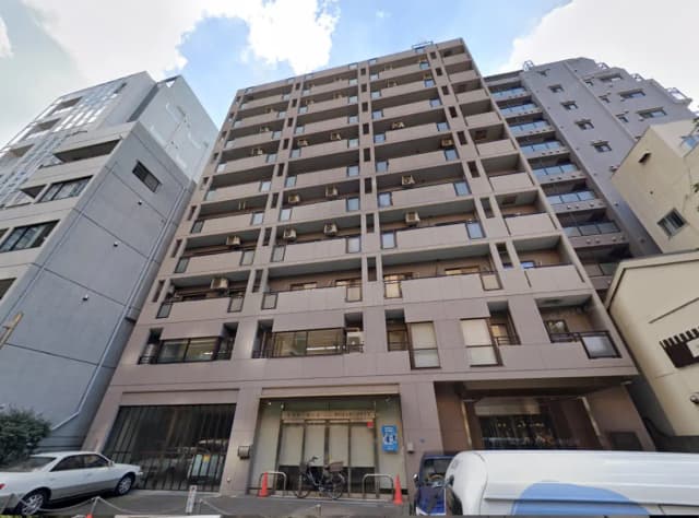 - 都市に立つ近代的なマンションの外観、複数の空調ユニットが設置され、周囲には駐車スペースが見える景観