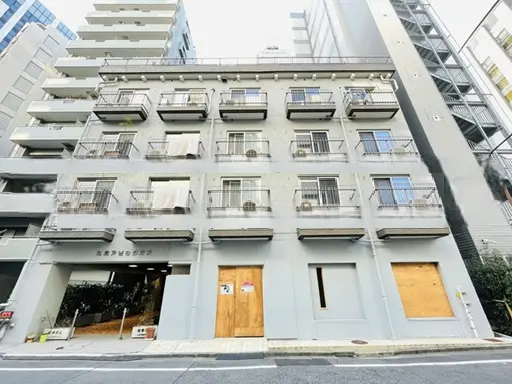 - 都市部に立つ外観が特徴的なアパートメントビル、各階にバルコニー、周囲は高層ビルに囲まれた住宅地区