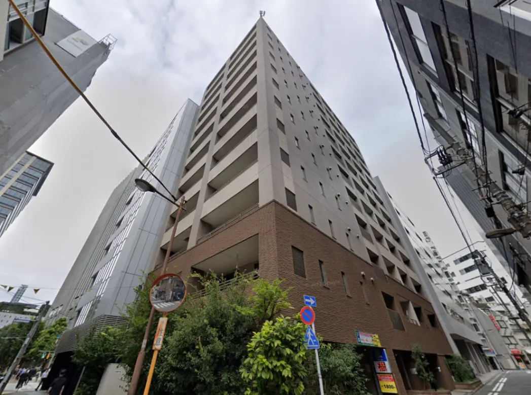- 高層ビルの外観、隣接する建物と道路、街路樹が見える都市の風景