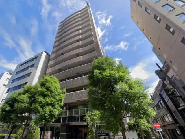 - 現代的なデザインの高層マンション、青空と緑豊かな街路樹が映える外観、隣接するビルとの調和が特徴的な風景