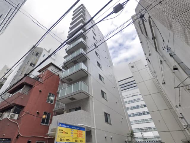 - 都市部に立つ近代的なマンション、周囲には他の建物と電線が見え、曇り空の下での景観