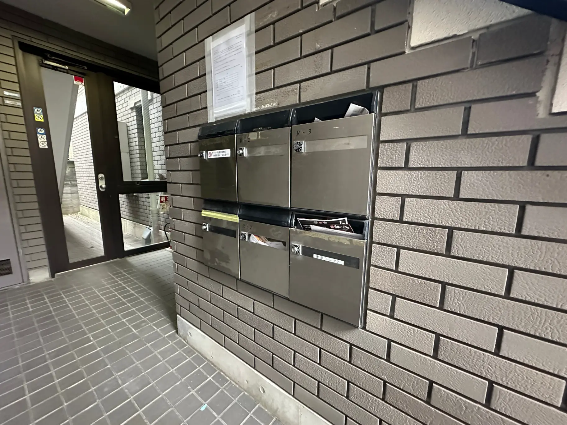 郵便受けが壁に埋め込まれたマンションのエントランスホール、灰色のタイルと赤レンガの壁