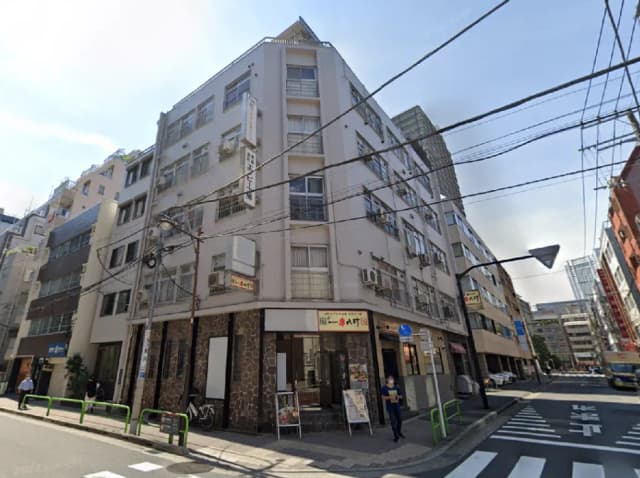 - 都市の一角にある商業ビル、周囲の建物や電柱が見える街並み、賑やかな通りの風景