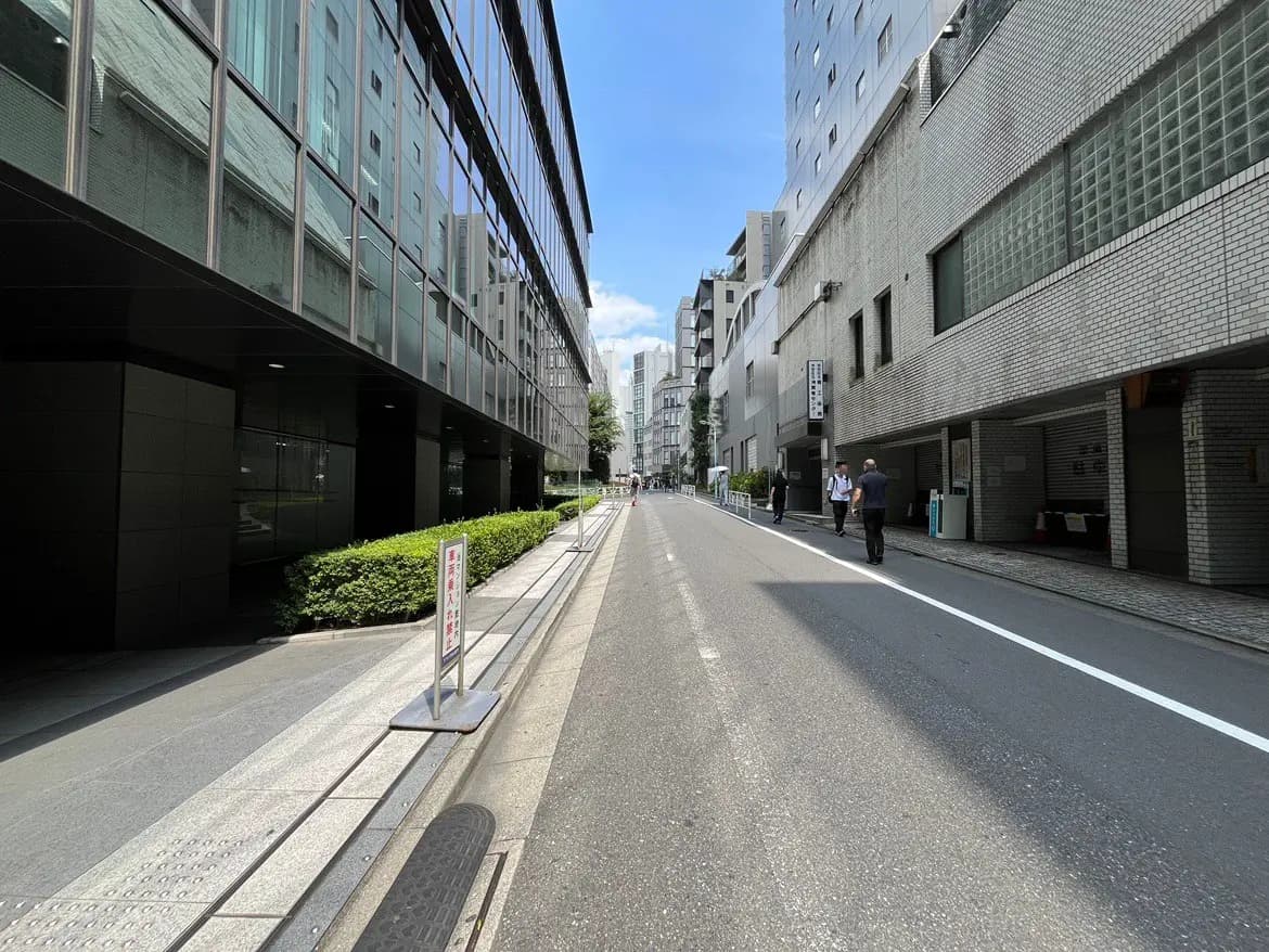 - 都市のビルが立ち並ぶ通り、青空が広がり、歩行者が行き交う様子を捉えた風景