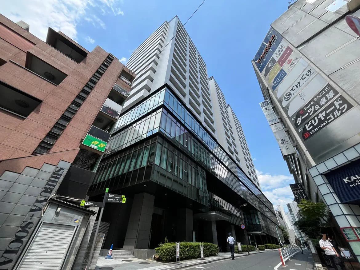 - 高層ビルと周辺の商業施設が立ち並ぶ都市の風景、青空とコンクリートのコントラストが鮮明な街並み