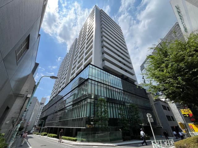 - 蒼い空の下、高層ビルの外観とガラス張りのファサード、周囲に人々が行き交う都市の風景