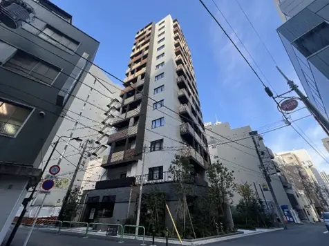 - 高層マンションの外観、周囲にはビルと街路樹がある都市の風景、青空を背景にしたタワー建築