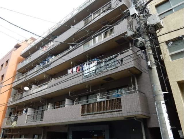 - 都市部のアパートメントビル、数階建ての外観、バルコニーに洗濯物が干されている様子と複雑な電線が見える