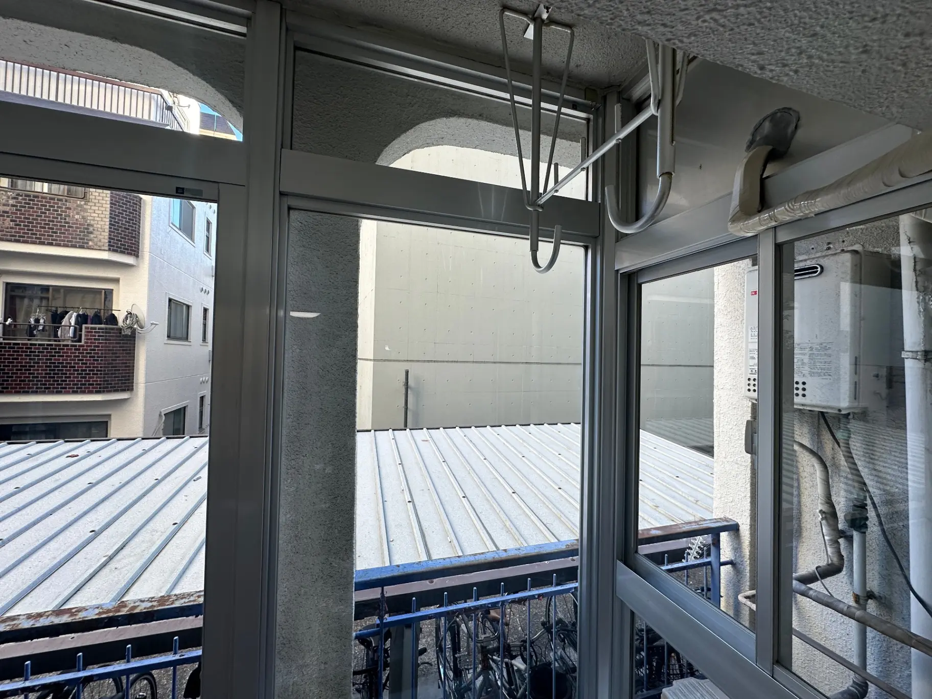 都市のアパートのバルコニー、グレーの壁と銀色の屋根、窓枠に水回りの配管が見える外観