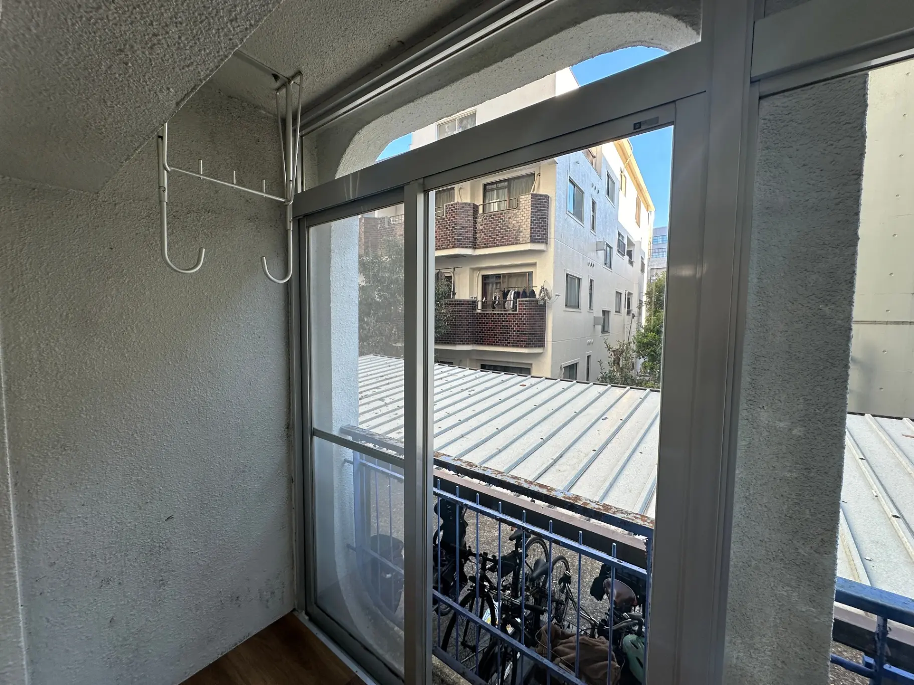 都市のマンションのバルコニー、スライドドアと壁にハンガーフック、向かいの建物の景色