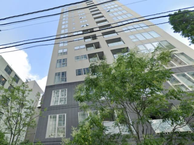 - 高層マンションの外観、周囲に緑の木々、青空を背景にした現代的なデザイン
