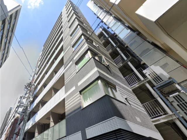 - 都市的な外観の高層マンション、各階にバルコニーと大きな窓、青空と隣接する建物が映る景観
