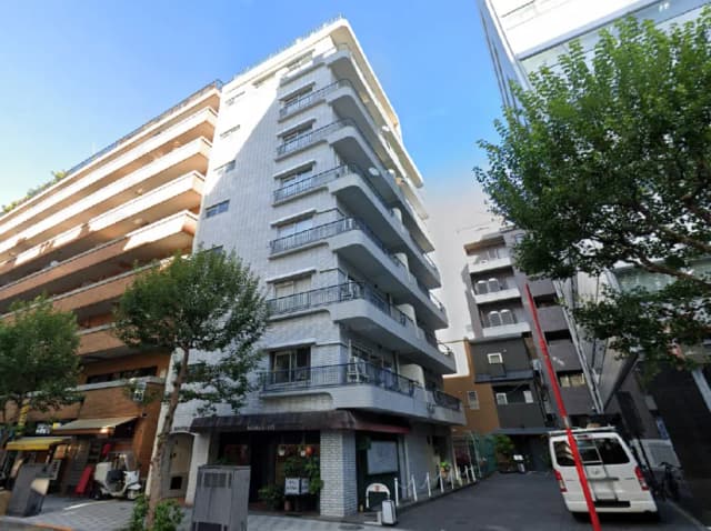 - モダンなデザインのアパートメントと周囲の建物、緑の木々と青空の背景が広がる住宅街の風景