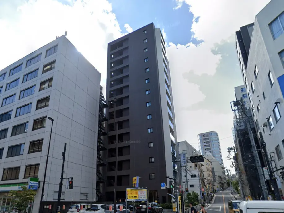 - モダンな外観の高層ビルと周囲の建物、青空が広がる都市風景、近くに交通信号機とパーキング看板が見える通り。