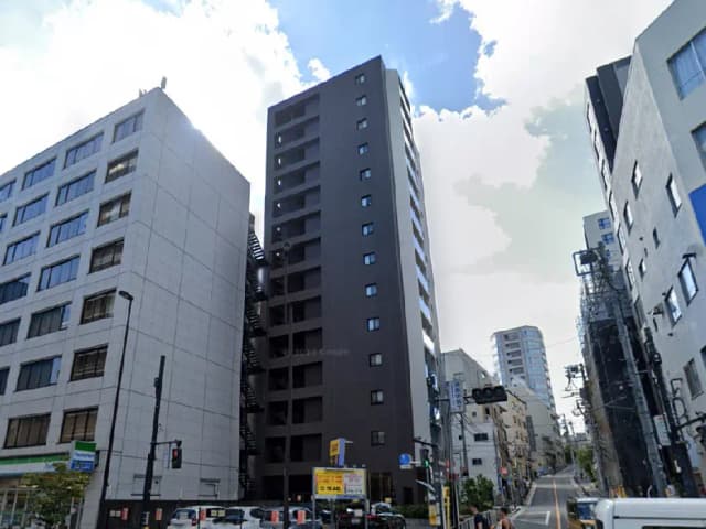 - モダンな外観の高層ビルと周囲の建物、青空が広がる都市風景、近くに交通信号機とパーキング看板が見える通り。