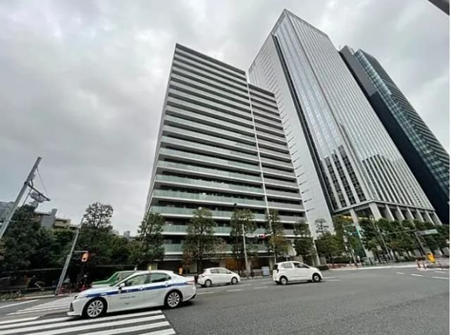 都市の交差点にあるモダンな高層ビル群、曇り空の下を走る車と歩行者の信号