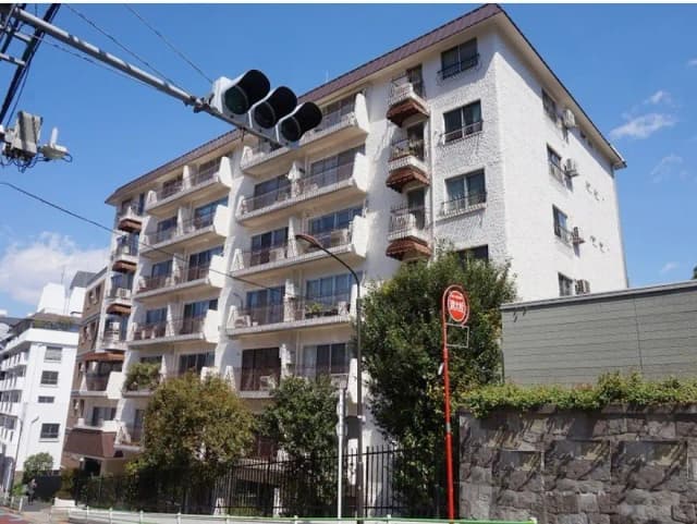 晴天の日に撮影された都市型マンションの外観、バルコニーに花が飾られた白い壁の建物