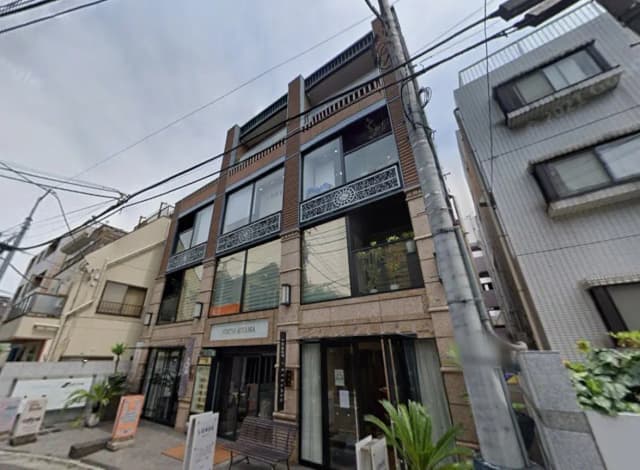 都会的な通りに面したモダンな外観のビル、一階には店舗があり、上階にはバルコニー付きの窓が特徴