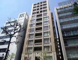 都市の風景に佇む現代的なマンションビル、青空と周辺の建物