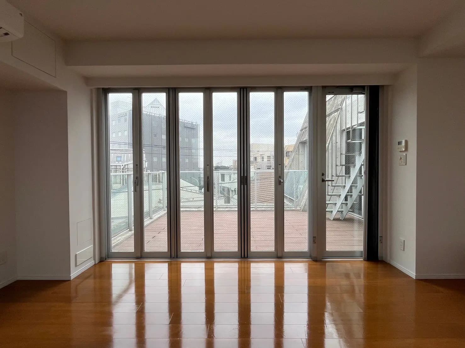 明るい木製フロアの部屋と大きな掃き出し窓、外には非常階段のあるモダンなアパートメント