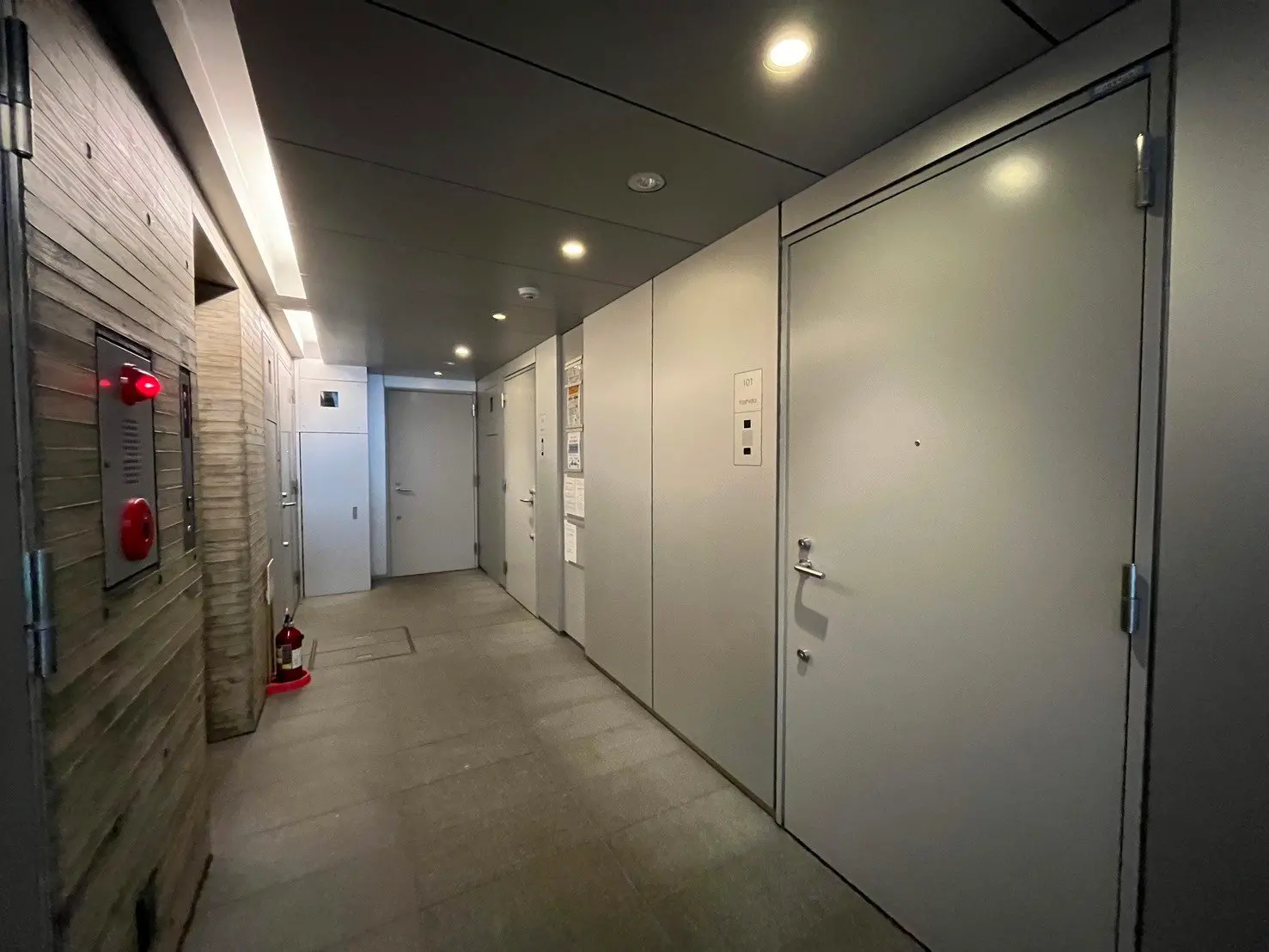 モダンな建物の内廊下、木目調の壁面、清潔感のあるフロア、非常灯と消火器が設置された安全設備