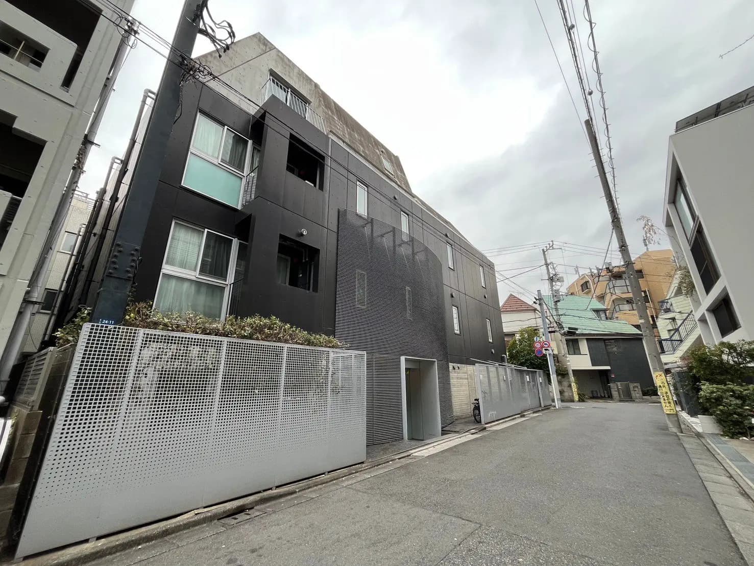 都会の住宅街にあるモダンな黒い外壁の建物、植栽が施されたバルコニー、静かな通りと配電線