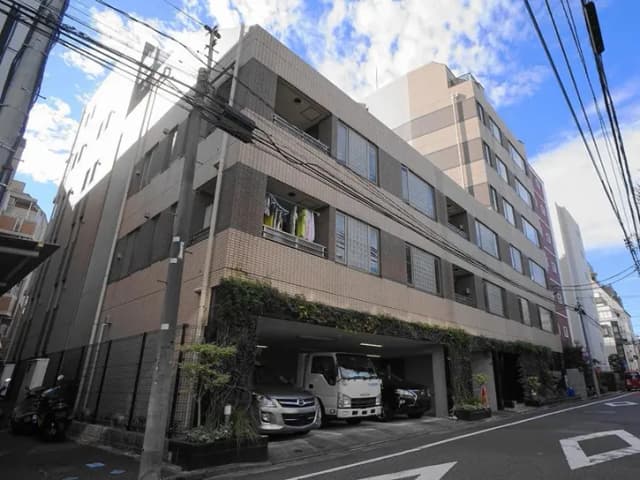 - 都市部にある現代的な建物の外観、駐車場に並ぶ車両やバルコニーに干された洗濯物が見える景色