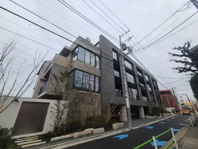 モダンな外観の都市型アパートメント、灰色の壁面とガラス窓、周囲に植樹が配された通り