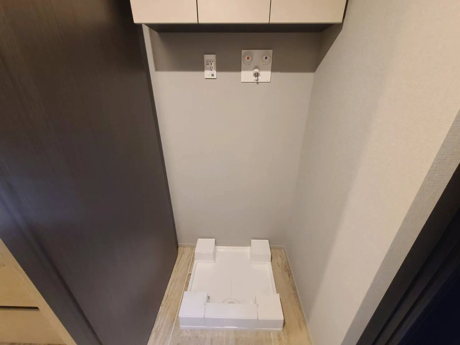 コンパクトな洗面所、ダークブラウンのキャビネット、ホワイトのカウンタートップ、壁には電源コンセント