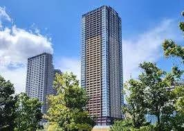 青空にそびえ立つモダンな高層マンション、緑豊かな公園の木々