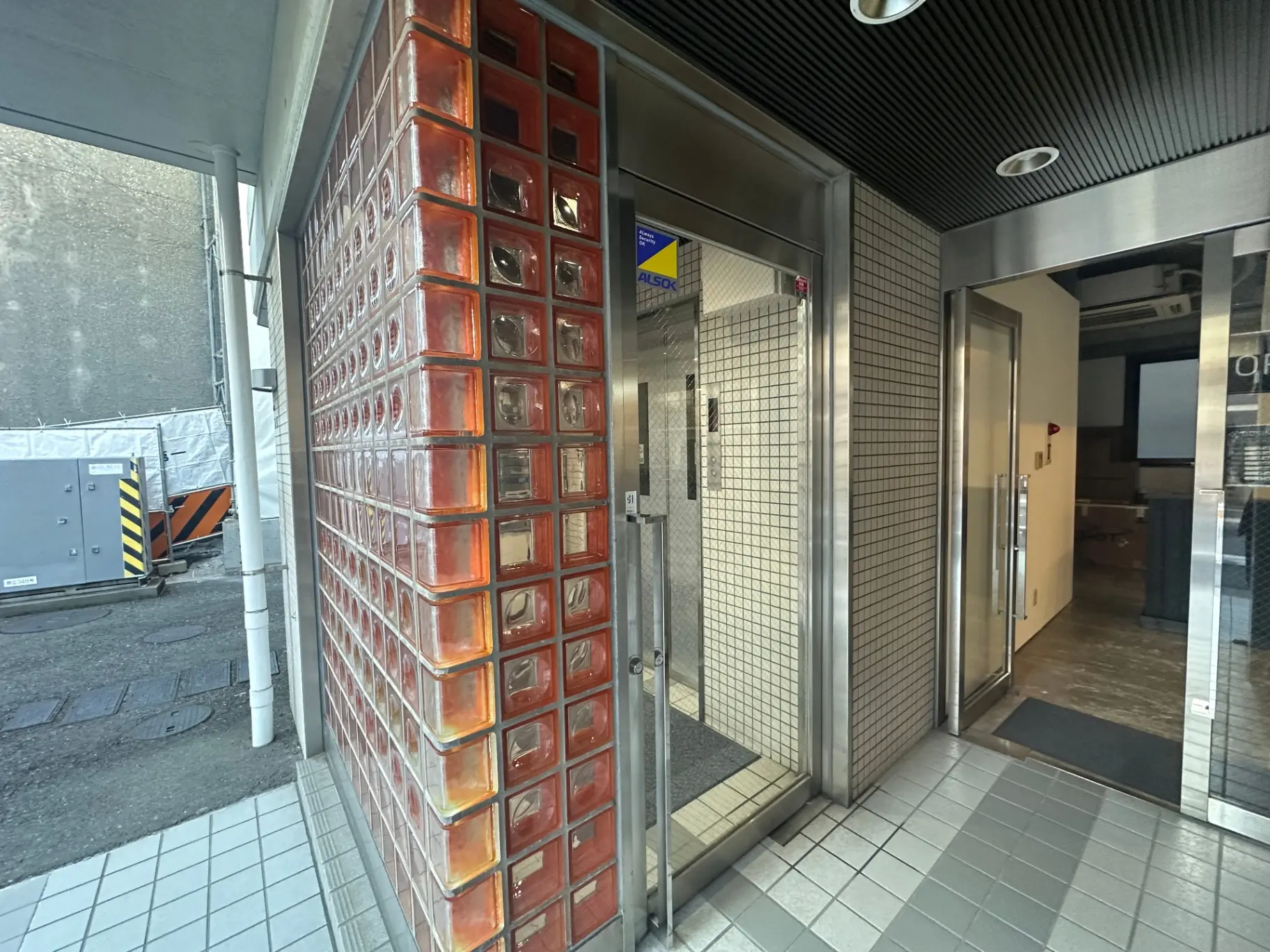 都会のビル内の入り口、赤いタイル壁とステンレス製のドア、清潔感のある外観デザイン