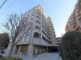 都市部に位置する現代的なマンションの外観、クリアな青空と周囲の緑、入口のアーチ状構造
