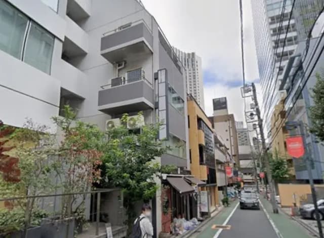 現代的な建築様式のアパートと周囲のビジネス街の景観、歩道に小さな緑の植栽がある都市の通り