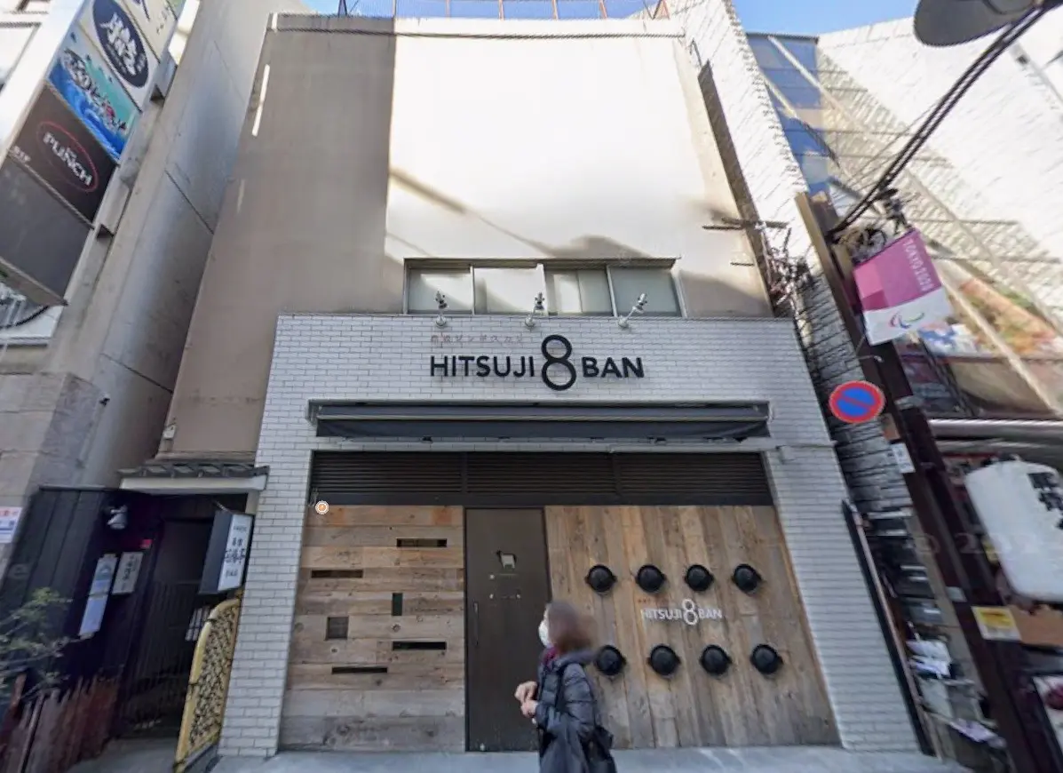 都会的な外観のビルにある「HITSUJI 8 BAN」と書かれた店舗、モダンなデザインの木製扉、人通りのある街角